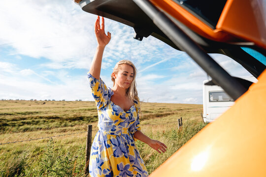 Woman steps out of a vehicle in a floral dress on a country road under a clear blue sky during daytime