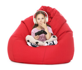 Surprised girl with controller and headphones playing video game on bean bag against white background © New Africa