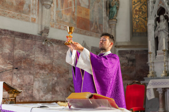 The priest holds the chalice high during a Holy Mass in a historic church in Europe, conducting the Eucharistic celebration and prayer.