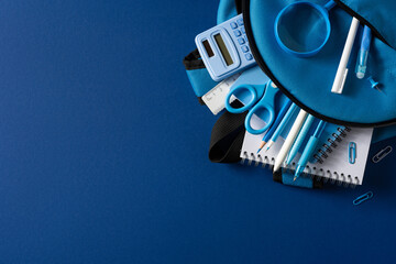 Naklejka premium Blue school supplies in a backpack arranged on dark background for back to school preparation
