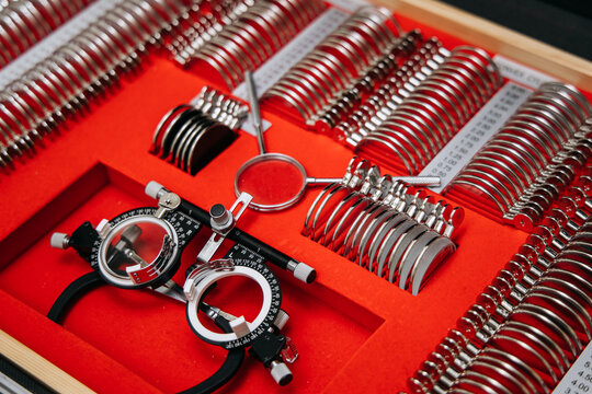 Optometry lens kit for assessing myopia and hyperopia with various lens rings and a trial frame on a bright red felt background in a wooden box