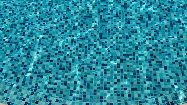 Blue mosaic tiles under clear swimming pool water.