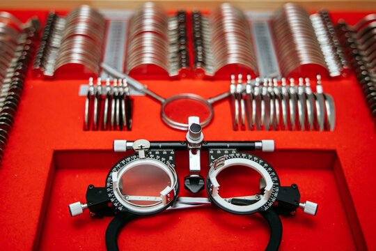 Optometry lens kit featuring phoropter, trial lenses, and accessories arranged on a red background for assessing myopia and hyperopia in patients