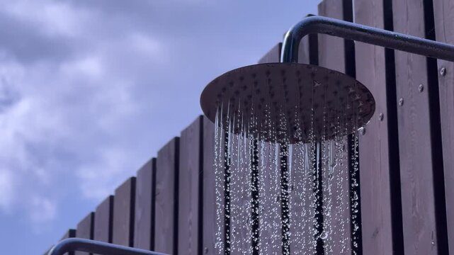 Water flowing from a modern outdoor rain shower against a contemporary wall, refreshing summer hygiene, resort lifestyle, wellness and travel concept.