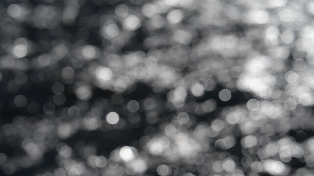 Moving water creates a bokeh sparkling abstract effect with beige light colored balls on a darker background
