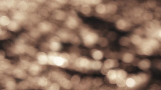Moving water creates a bokeh sparkling abstract effect with beige light colored balls on a darker background
