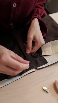 Close-up shot of a tailor carefully testing the zipper and aligning a metal clasp on the waistband of dark brown trousers. Apparel construction, custom tailoring tutorials, fashion design courses