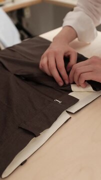Close-up shot of a tailor carefully testing the zipper and aligning a metal clasp on the waistband of dark brown trousers. Apparel construction, custom tailoring tutorials, fashion design courses
