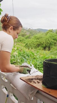 Vertical video. Woman Wearing Protective Gloves Holds Dark Soil beside a Black Fabric Pot, Preparing Fertile Substrate for Growing Plant Outdoors