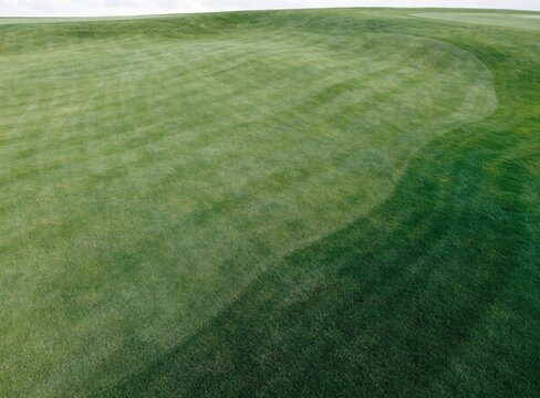 Aerial perspective of a lush green golf course fairway featuring rolling terrain and meticulously groomed grass patterns under natural daylight