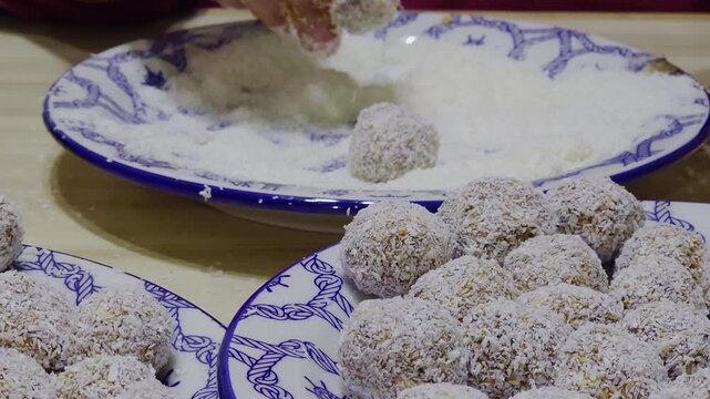 Female hands making delicious chocolate, oatmeal and coconut bonbons, rolling them in grated coconut