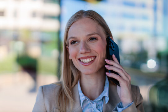 businesswoman is talking on her phone with a smile while standing outside in a city