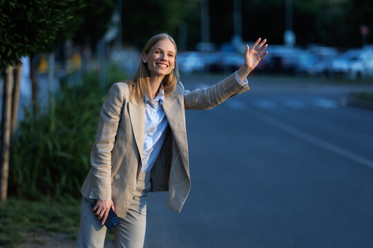 Young blonde businesswoman hailing a taxi on a city street during the evening