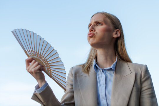 Businesswoman using a fan while standing outdoors during a sunny, hot day