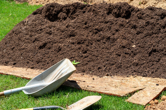 Large pile of dark, rich organic soil or compost ready for gardening and planting, with a shovel and trowel resting on wood, symbolizing outdoor yard work and soil preparation.