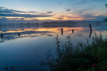 Obraz premium Wooden posts in lake under colorful sunset sky