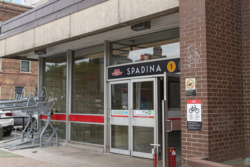 Obraz premium Toronto, ON, CANADA - Aug 8 2024 : Entrance to the TTC Spadina subway station in Toronto with a sign, a yellow Line 1 marker, glass doors with a red stripe, a bicycle repair stop notice.