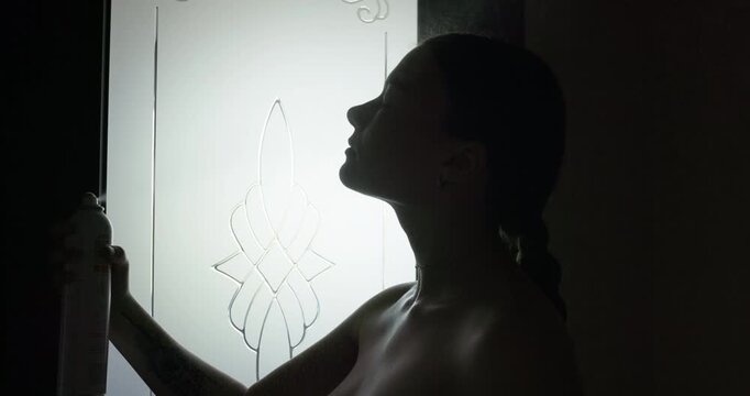 Silhouette of young topless woman spraying thermal water or face mist, slow motion