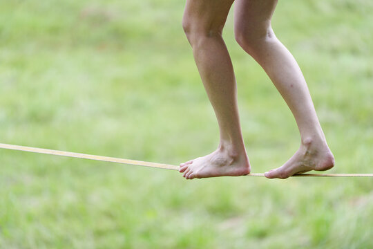 Bare feet walking on slackline over green grass, staying on track focus and one step at a time life balance concept.