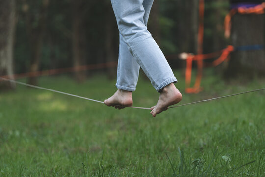 Bare feet gripping orange slackline between trees, finding balance and staying grounded in life wellness and mindfulness concept.