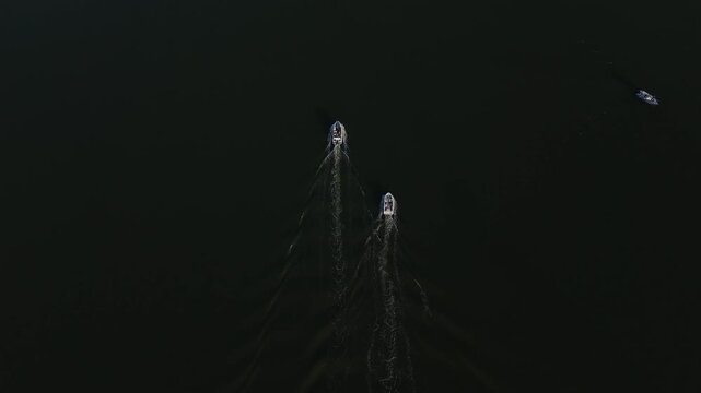 Drone footage from directly above of two speedboats moving across calm dark water with matching white wakes forming a striking geometric pattern