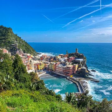 Colorful coastal village of Vernazza with its traditional houses, harbor, and Doria castle, located in the Cinque Terre National Park, Liguria, Italy, under a bright blue sky.