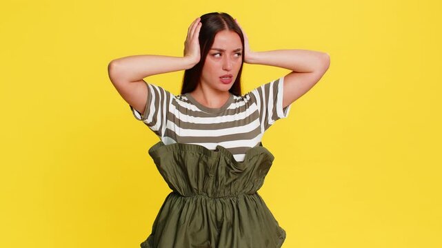 Woman covering ears with hands and grimacing, clearly refusing to hear bad news or unpleasant information. Girl on yellow background expresses emotional rejection and unwillingness to listen further.
