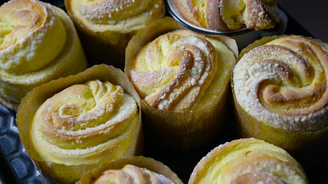 Freshly baked cruffins with cream filling. Delicious homemade cruffins, a hybrid of croissant and muffin, with a creamy vanilla filling and a dusting of sugar, sitting on a dark baking tray