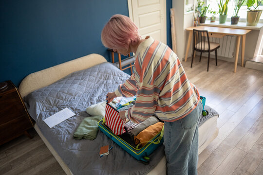 Woman traveler finishing packing personal belongings in suitcase for planned vacation journey, attentive female neatly putting clothes and accessories inside case, routine traveling preparations.
