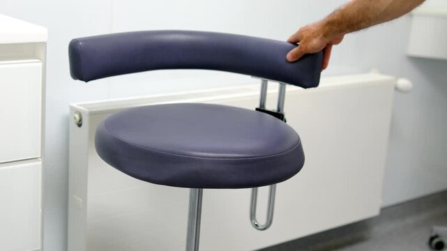 a man hand touches a chair Dental assistant stool beside treatment workstation in modern dentistry clinic clean professional interior