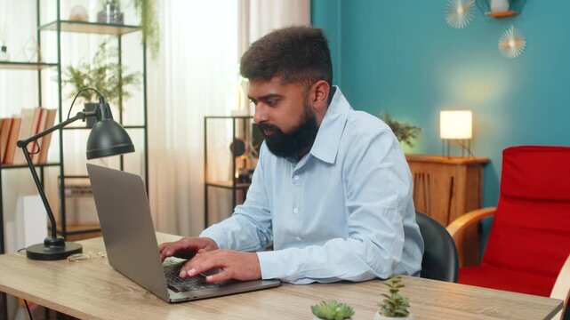 Indian man at home shuts laptop rotates neck muscles feels pain after overtime duty needs stretch. Arabian guy at desk rubs shoulders shows tired eyes seeks relief relaxes slowly recovering energy up.