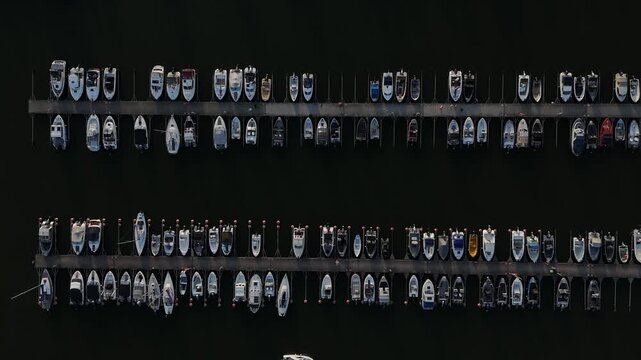 Top drone perspective of marina with parallel docks and numerous boats creating clean symmetrical composition beside the coastline