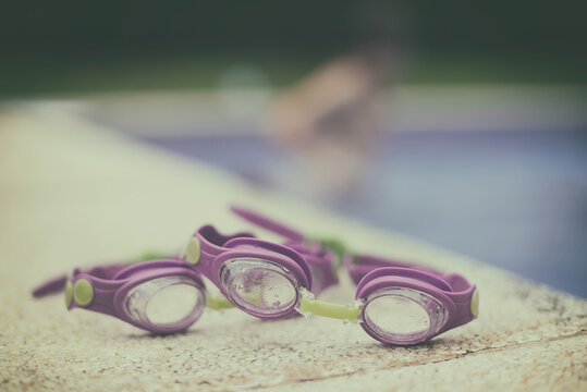 Close-up of two pairs of Swimming goggles at the edge of a swimming pool with a person in the background