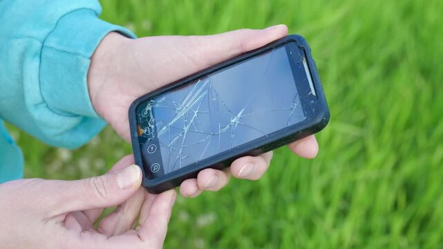 Person holding a smartphone with a broken screen. Worried person holding a modern smartphone with a completely shattered and cracked screen after an accident, showing the need for repair
