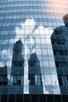 Tall glass skyscrapers of business offices in city reflect blue sky, clouds, and other skyscrapers. Sunlight glistens on glass surface. modern cityscape of  city's business district. vertical