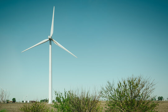 Close-up of a wind turbine rising above rural farmland and green shrubs
