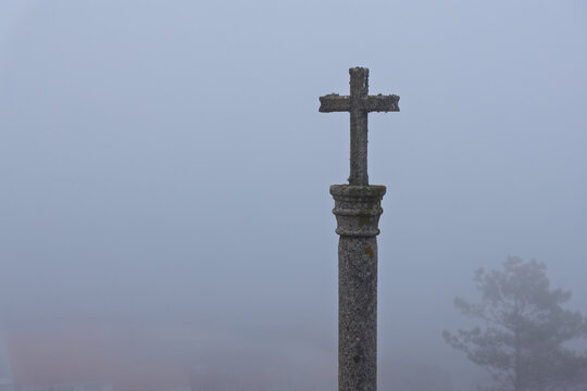 Stone christian cross standing in dense fog