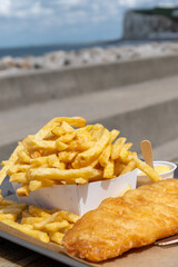 Fototapeta premium Fish and chips on Le Treport promenade — golden battered cod with mountain of french fries, seaside flavors enjoyed outdoors by the harbor in Normandy, France