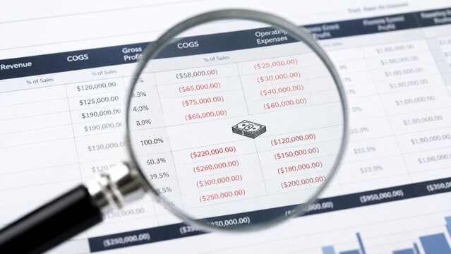 Magnifying glass focusing on red financial numbers on a paper spreadsheet