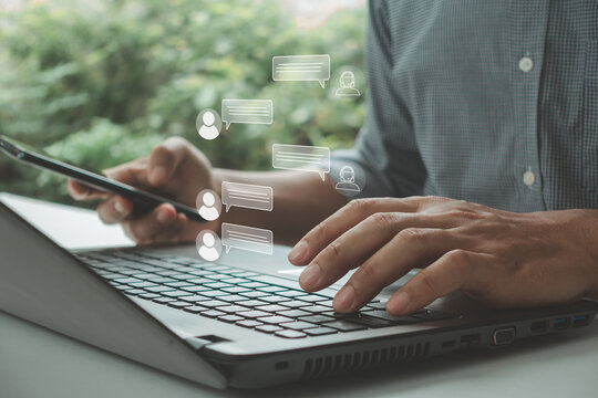 Businessman using laptop, smartphone with online chat, customer support icon. Concept of digital communication, live chat service, virtual assistance, messaging technology, remote customer service.