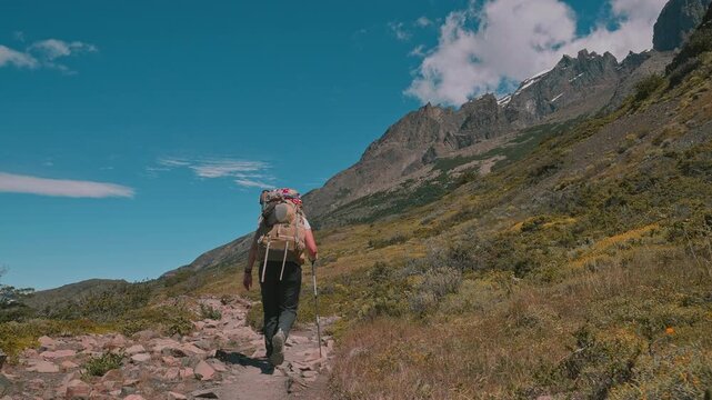 Following behind a backpacking hiker on the Torres del Paine W Trek with mountains and blue skies, Patagonia, Chile