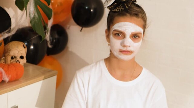 A cute teenage girl is getting ready for Halloween and doing face painting, with a skeleton painted on her face. October is a time of horror.