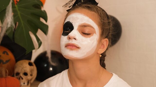 A cute teenage girl is getting ready for Halloween and doing face painting, with a skeleton painted on her face. October is a time of horror.