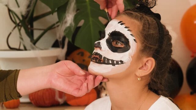 A cute teenage girl is getting ready for Halloween and doing face painting, with a skeleton painted on her face. October is a time of horror.