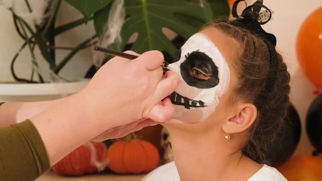 A cute teenage girl is getting ready for Halloween and doing face painting, with a skeleton painted on her face. October is a time of horror.