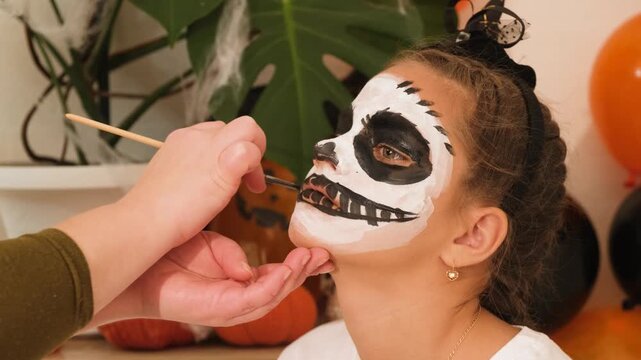 A cute teenage girl is getting ready for Halloween and doing face painting, with a skeleton painted on her face. October is a time of horror. makeup artist concept