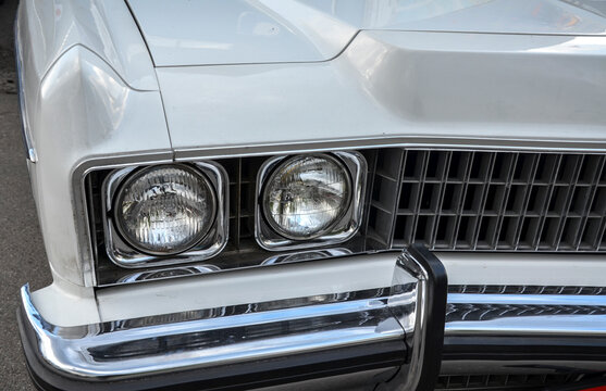 Close-up of a classic white Chevrolet Caprice front fascia, featuring dual round headlights in square chrome housings, and a gleaming chrome bumper with a black guard