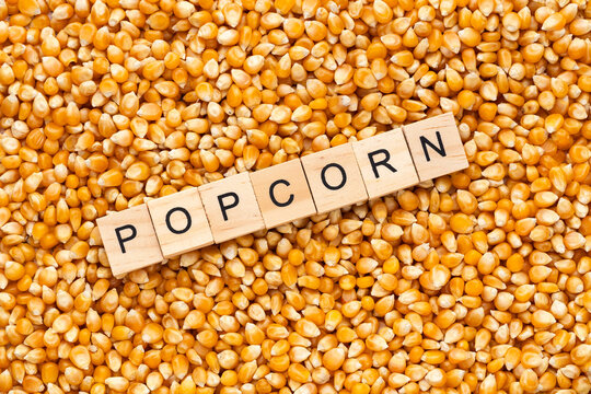Popcorn kernels arranged around wooden blocks spelling out "POPCORN," ideal for food and entertainment concepts.