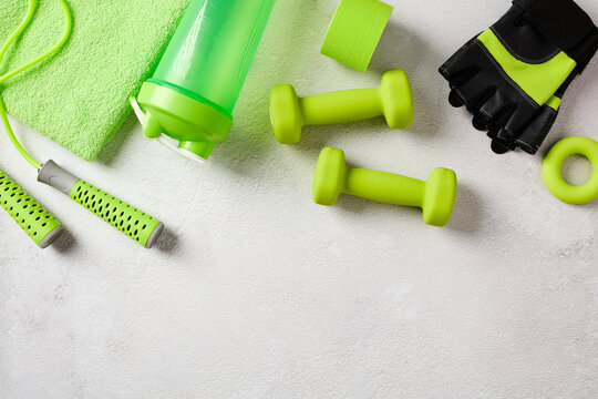 Green gym equipment and fitness accessories arranged at the top of a textured concrete background with empty space below. Flat lay.