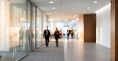 Fototapeta premium A modern office corridor with blurred figures walking. The space features glass walls and wooden accents, creating a professional ambiance.
